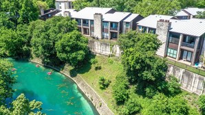 Un hôtel moderne composé de plusieurs bâtiments, situé au bord d’une rivière et entouré d’une végétation luxuriante.