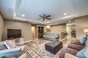 A spacious living room with a flat-screen TV, a ceiling fan, and a large rug.