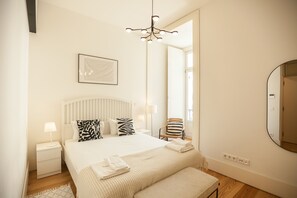 A hotel room with a bed, bedside tables, a chair, a mirror, and a chandelier.