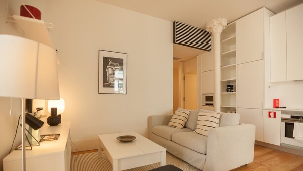 A modern living room with a sofa, a small table, a lamp, and a framed picture on the wall.