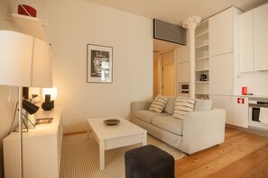 A modern living room with a sofa, a small table, a lamp, and a framed picture on the wall.