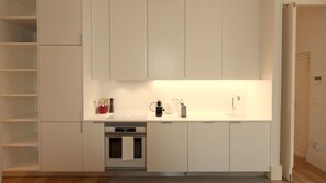 A compact kitchen with white cabinetry, a built-in oven, and a countertop with a coffee maker and toaster.