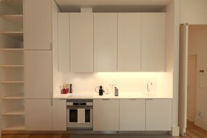 A compact kitchen with white cabinetry, a built-in oven, and a countertop with a coffee maker and toaster.