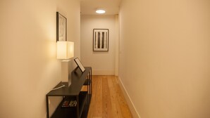 A hallway with a piano, framed artwork, and a lamp.