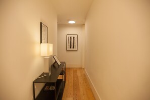A hallway with a piano, framed artwork, and a lamp.