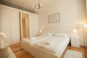 A modern hotel room with a double bed, bedside lamps, a large mirror, and a ceiling light fixture.