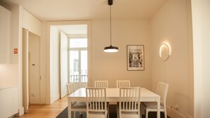 A dining area with a white table and chairs, a pendant light, a framed picture on the wall, and a door leading to another room.