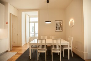 A dining area with a white table and chairs, a pendant light, a framed picture on the wall, and a door leading to another room.