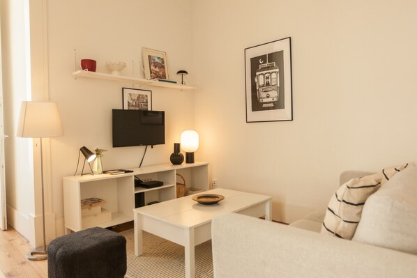 Una sala moderna con sofá, mesa de centro, televisor y lámpara.
