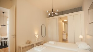 A bedroom with two beds, a vanity with a mirror, a bench, and a hanging light fixture.