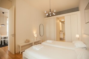A bedroom with two beds, a vanity with a mirror, a bench, and a hanging light fixture.