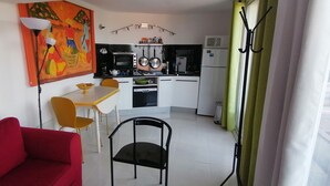 A compact kitchen with a dining area, a red sofa, and a colorful painting on the wall. - Studio with pool 5 minutes from Hyères beaches. Extraordinary view! (Hyères)