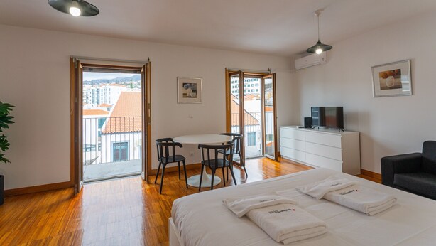 Une chambre d’hôtel équipée d’un lit, d’un bureau, de chaises, d’une télévision et d’un balcon offrant une vue sur les bâtiments.