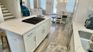 Una cocina moderna con armarios blancos, una isla central con estufa y una zona de comedor con mesa y sillas.