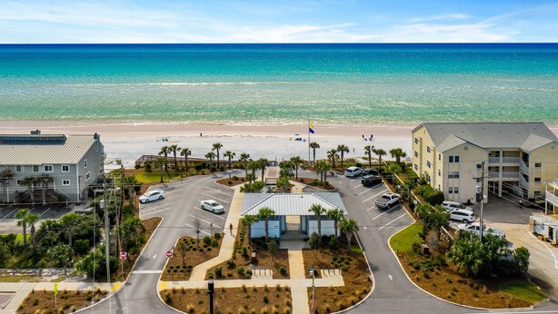 Un hotel frente a la playa con estacionamiento, una playa al fondo y cielo despejado.