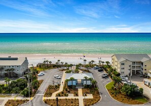 A beachfront hotel with a parking lot, a beach in the background, and a clear sky. - Beach home w/ 6 seater golf cart, walk to the beach/pool/fast internet (Santa Rosa Beach)
