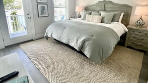 Un dormitorio con cama, ventilador de techo, mesita de noche, lámpara y vistas al exterior.