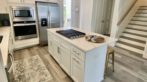 Una cocina moderna con armarios blancos, electrodomésticos de acero inoxidable, una isla central con estufa a gas y piso de madera.
