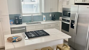 Una cocina moderna con muebles blancos, un refrigerador de acero inoxidable, horno empotrado y cafetera. Hay tres taburetes dorados en la isla.