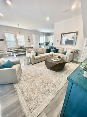 Un salon spacieux comprenant un grand canapé d’angle, une table basse et un coin repas avec une banquette et une table.