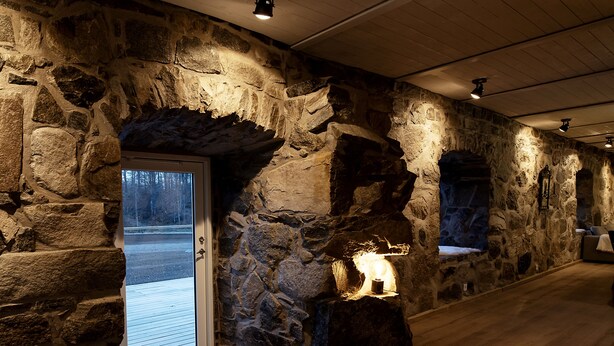 Ein Innenraum mit Steinwänden und Holzboden, eine Glastür zum Außenbereich und ein beleuchteter Kamin aus Stein.