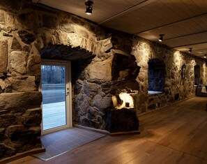 Et interiør med stenvægge, trægulv, en glasdør der fører udendørs, og en oplyst stenspir.