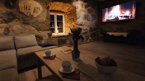 Ein gemütlicher Raum mit Steinsäulen, einer Couch, einem Holztisch mit Tasse und Untertasse, einer Vase mit Blumen und einer Fruchtschale.