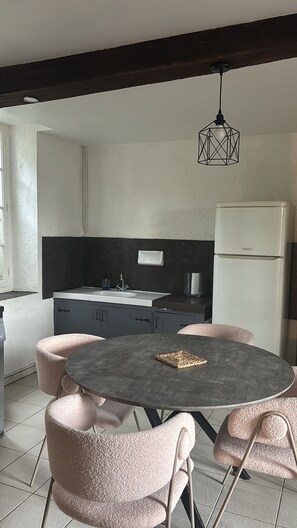 A compact kitchen with a round table and pink chairs, a white refrigerator, and a hanging light fixture. - Peaceful cottage with small pool (Mongauzy)