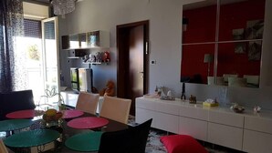 Un coin repas avec une table dressée pour quatre personnes, une cuisine avec un plan de travail rouge et un grand miroir au-dessus du comptoir.