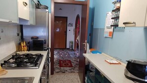Une cuisine compacte équipée d’une cuisinière à gaz, d’un four à micro-ondes et d’un évier. On y trouve également un petit réfrigérateur et une machine à café. La cuisine a un sol carrelé et une porte qui donne sur une autre pièce.