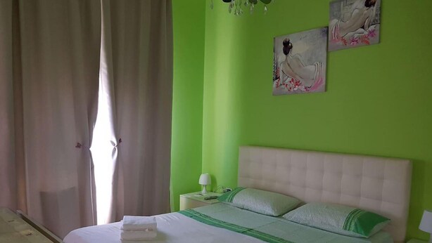 Une chambre avec un mur vert, un lit blanc agrémenté de touches de vert, une table de chevet avec une lampe et un tableau au mur.