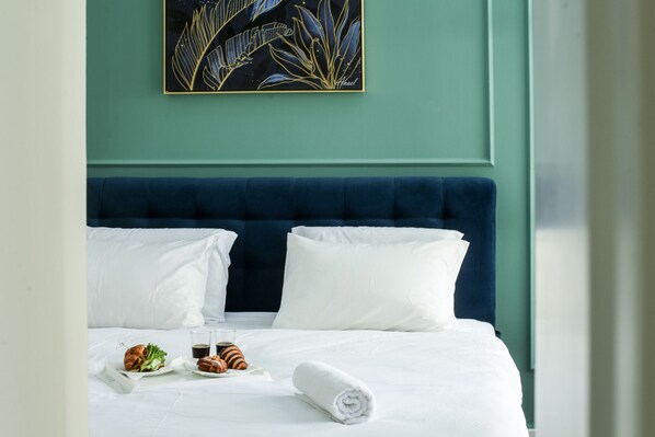 A neatly made bed with white linens, a blue headboard, and a painting above it.