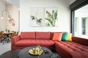 A modern living room with a red sectional sofa, a round coffee table with a tray, and two framed botanical prints on the wall.