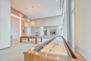 A modern interior with a shuffleboard table, wooden furniture, and pendant lighting.