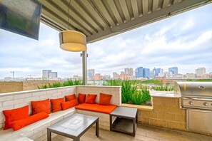 An outdoor patio with a seating area, a grill, and a view of the city skyline.
