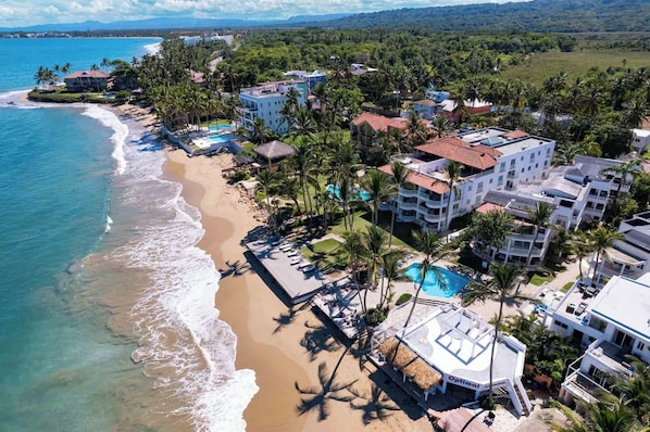 A coastal resort with beachfront villas, a swimming pool, and palm trees.