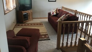 A living room with a TV, a sofa, and a wooden staircase. - Ski and Golf Retreat by Hole 8 (Clymer)