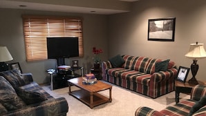 A living room with a plaid sofa, a coffee table, a television, and a framed picture on the wall. - Ski and Golf Retreat by Hole 8 (Clymer)