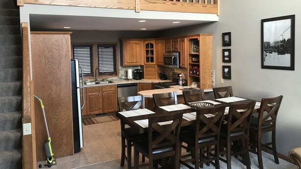 A modern kitchen with wooden cabinets, a dining area with a table and chairs, and a staircase leading to an upper level. - Ski and Golf Retreat by Hole 8 (Clymer)