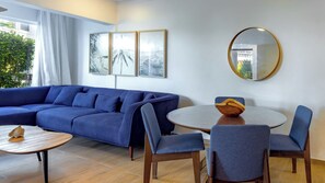 Een moderne woonkamer met een blauwe modulaire bank, een ronde eettafel met stoelen, een houten schaal als decoratie en drie ingelijste kunstwerken aan de muur.