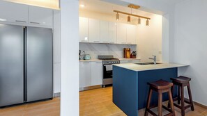 Een moderne keuken met een roestvrijstalen koelkast, een gasfornuis en een achterwand van marmer. Er staan houten krukken bij een blauw kookeiland met een spoelbak.