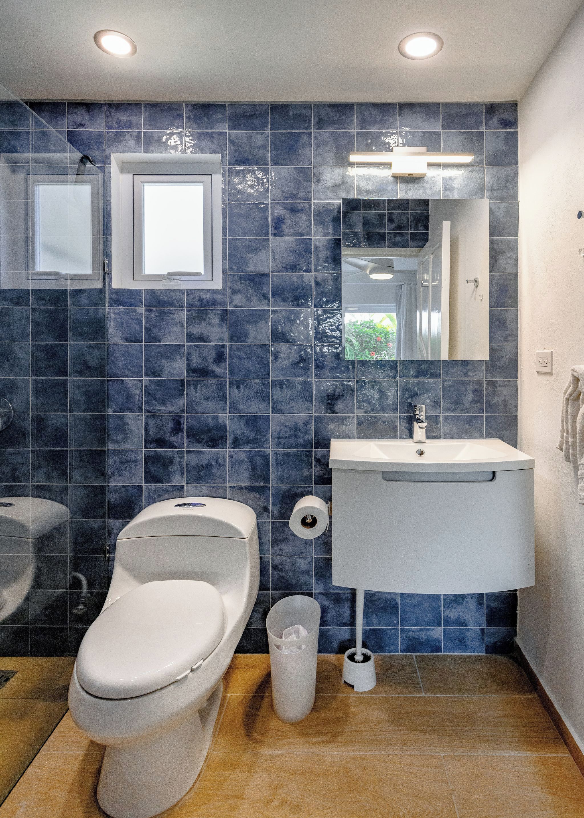Un baño con inodoro, bidé, lavamanos, espejo y paredes con azulejos azules.