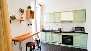A kitchen with green cabinets, a black countertop, and a wooden bar stool. - A break somewhere! (Marseille)