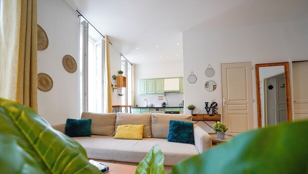 A modern living room with a sofa, green plants, and a view into the kitchen. - A break somewhere! (Marseille)