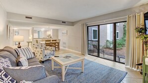 Ein Wohnzimmer mit einer Couch, einem Couchtisch und Blick ins Freie durch eine Schiebetür.