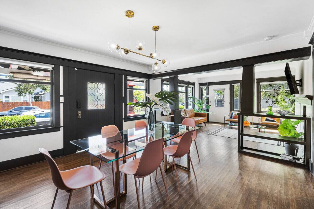 A modern dining area with a glass table and metal chairs, large windows, and a black-framed door.