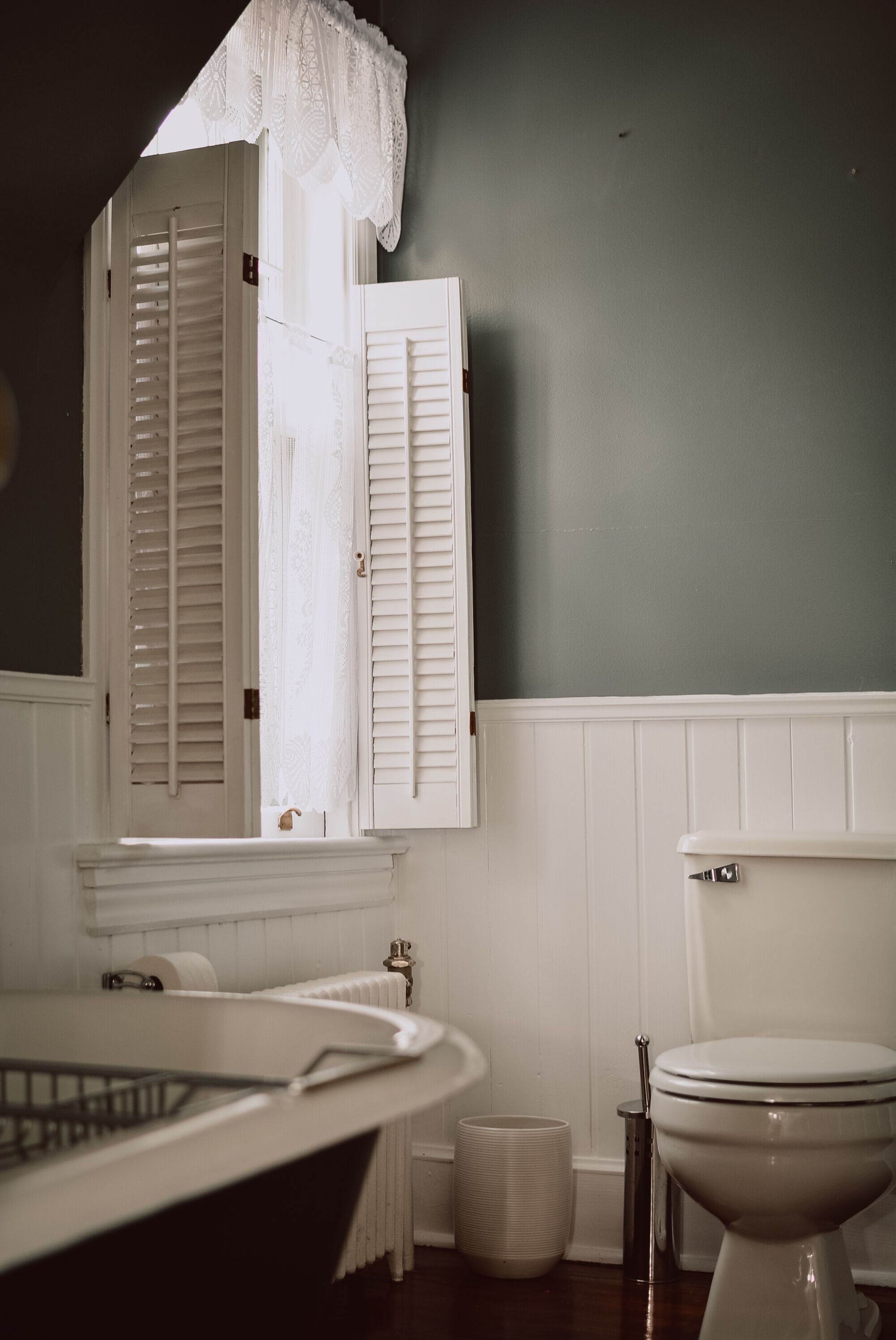 A bathroom with a white bathtub, a toilet, and a window with white shutters.