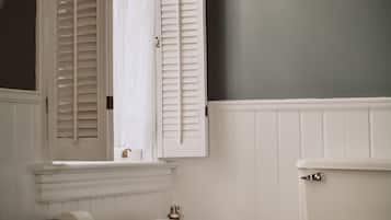 A bathroom with a white bathtub, a toilet, and a window with white shutters.