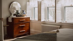 Ein Schlafzimmer mit einem Holzkasten, einem runden Spiegel und einem Fenster mit Läden.