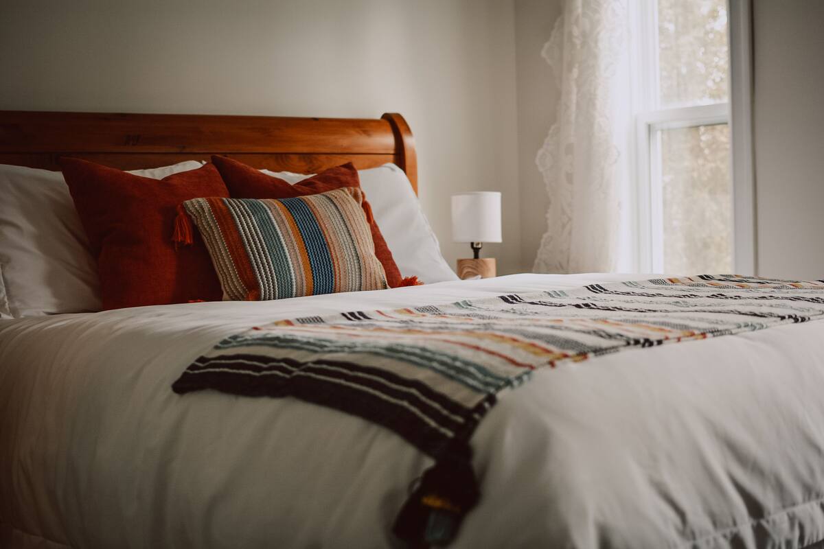 Una cama bien tendida con un edredón a rayas, varios almohadones y una mesita de noche con una lámpara.